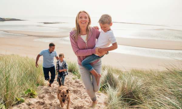 A family walking up a sand dune away from the sea with their dog