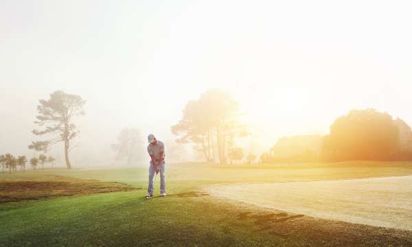 Man playing golf on beautiful course with sun rising in the background