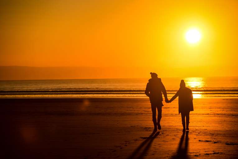 A couple walking across a beach in winter at sunset