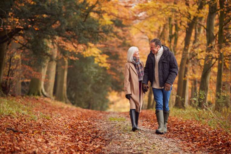 A mature couple walking along a woodland lane in the middle of autumn