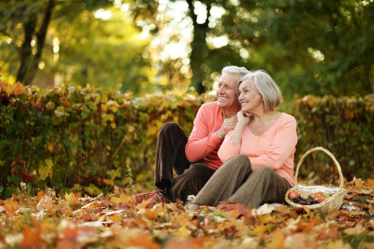 A mature couple sitting in the autumn countryside with a picnic