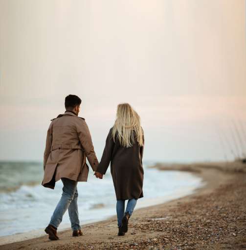 A couple walking hand in hand along a beach in winter