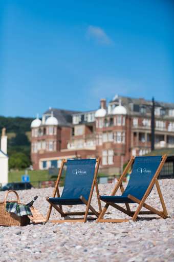 Deck chairs on pebble Sidmouth beach Victoria Hotel in background