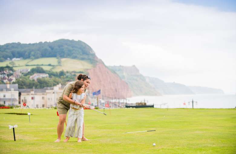 mother and daughter playing on putting green at the Victoria hotel with jurassic coast in the background