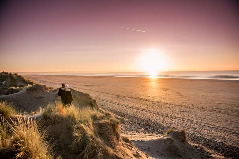 Couple on the beach during a sunset looking from the dunes