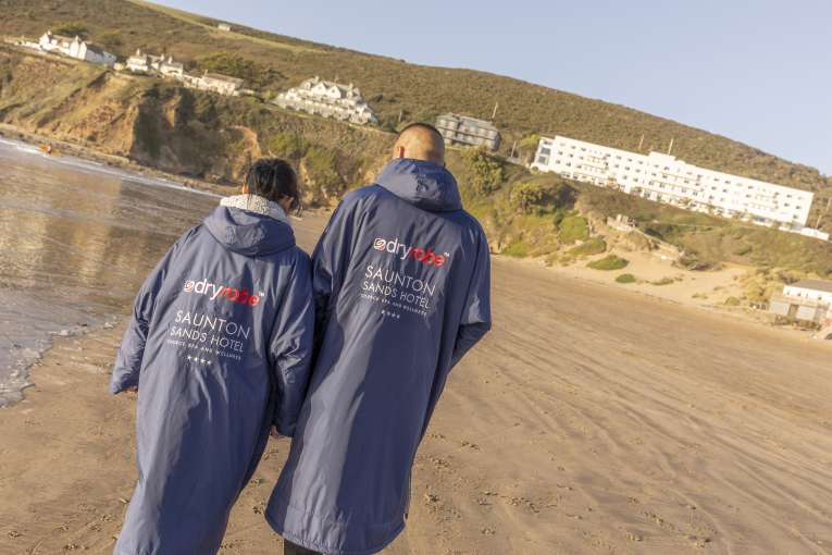 Couple walking on the beach wearing one of our branded Dryrobes