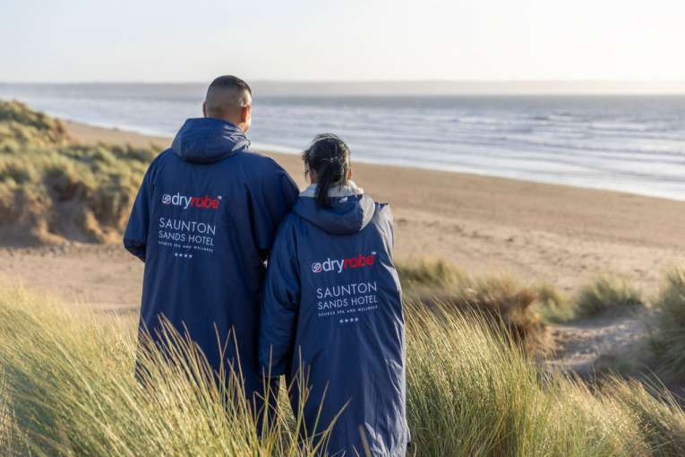 Couple standing on the beach with their branded Saunton Sands Hotel dryrobes on
