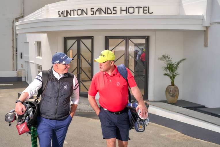 Two Men with their golf clubs walking to the camera outside Saunton Sands Hotel 