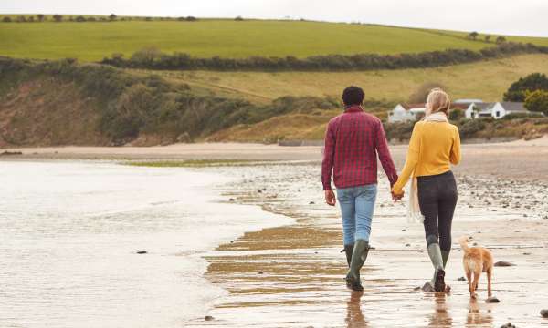 A couple walking along a beach with their dog in winter
