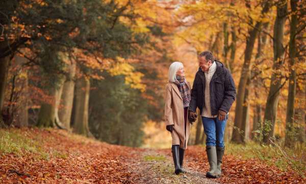 A mature couple walking along a woodland lane in the middle of autumn