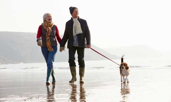 A mature couple walking their dog along the beach in winter