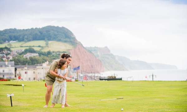 mother and daughter playing on putting green at the Victoria hotel with jurassic coast in the background