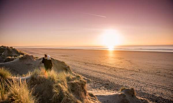 Couple on the beach during a sunset looking from the dunes