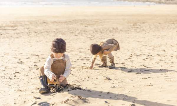 Two children on the beach during autumn playing with the sand 