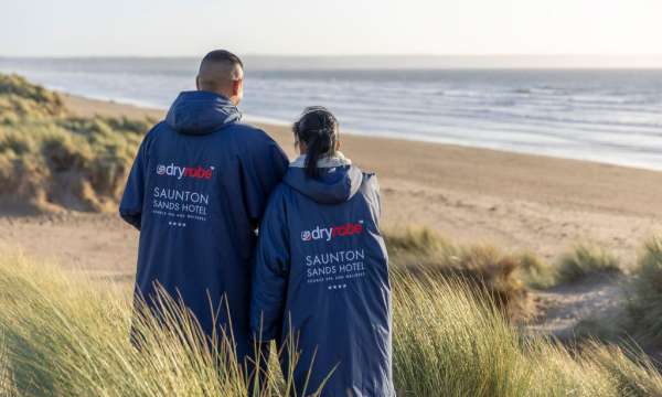 Couple standing on the beach with their branded Saunton Sands Hotel dryrobes on