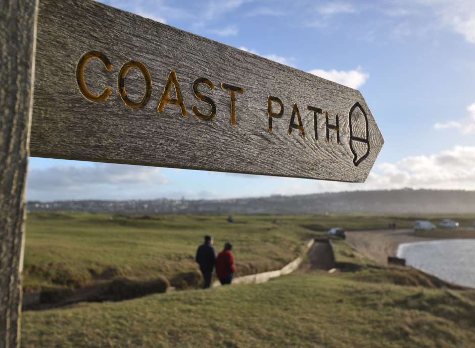A coast path sign with a couple in the background