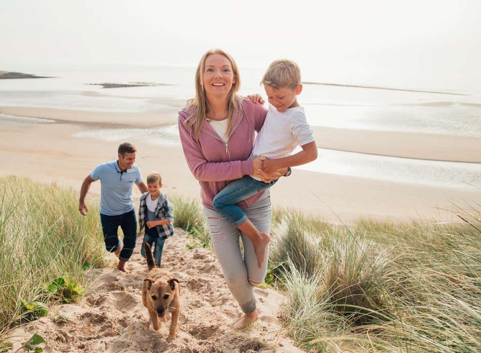 A family walking up a sand dune away from the sea with their dog