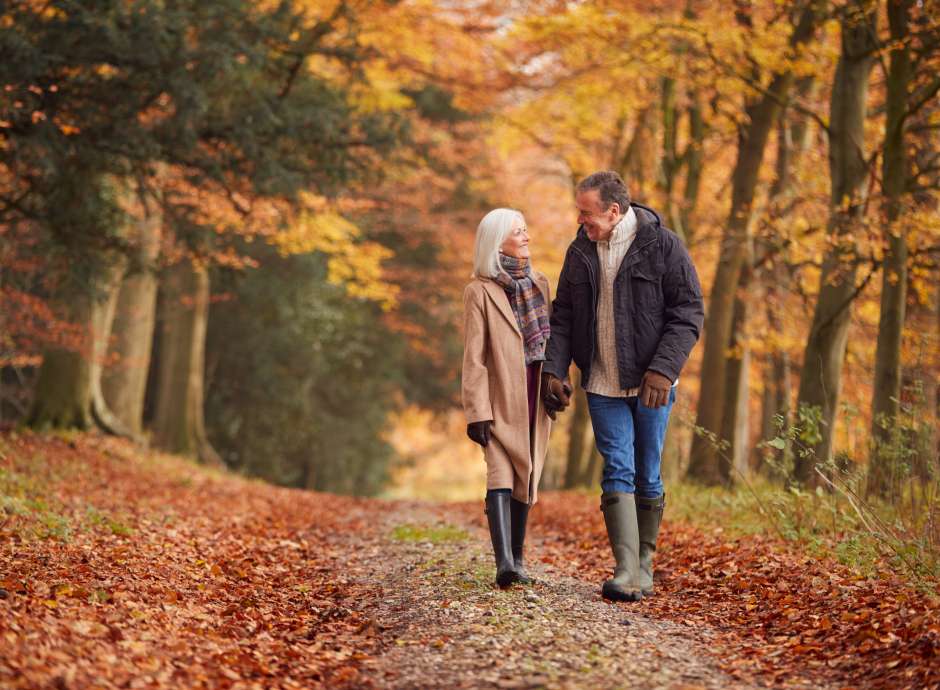 A mature couple walking along a woodland lane in the middle of autumn