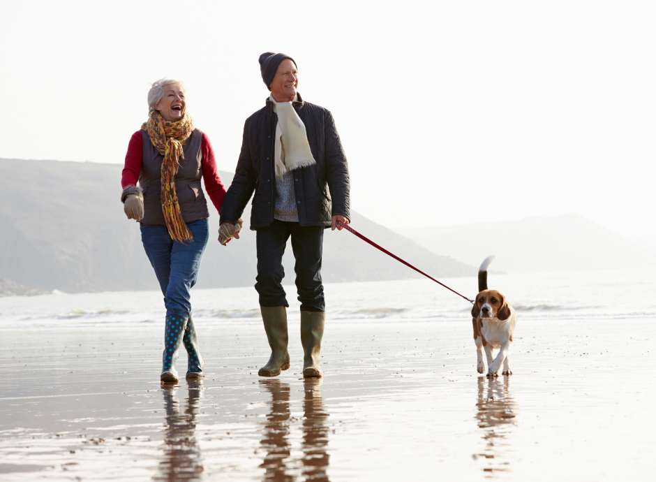 A mature couple walking their dog along the beach in winter