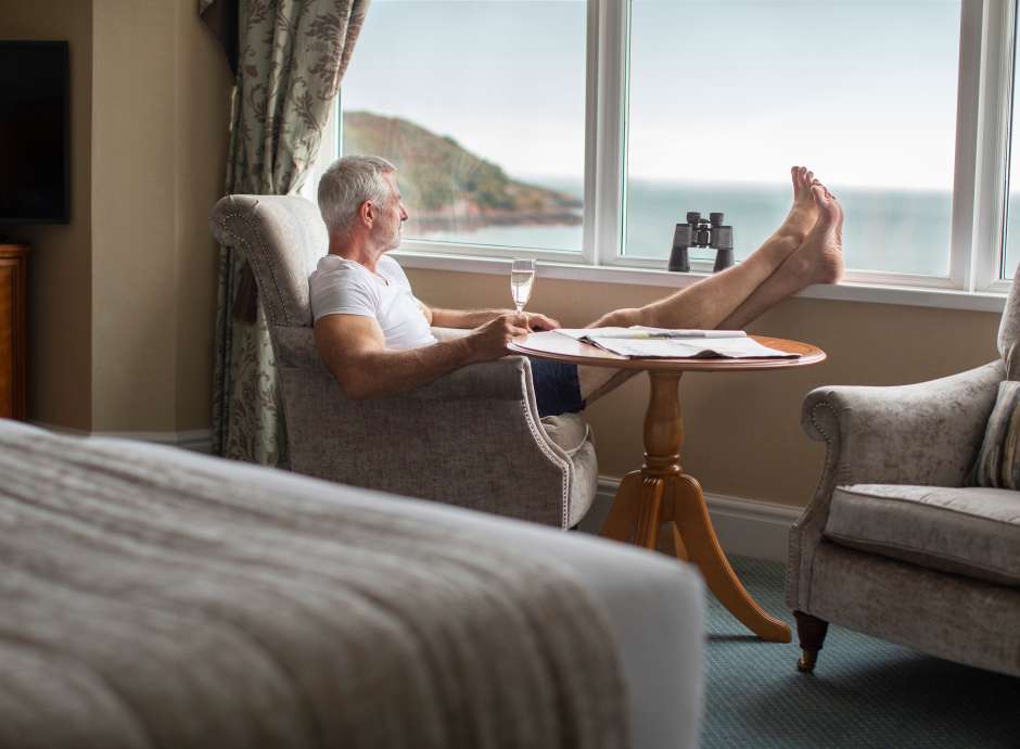 man relaxing with feet up sea view room with prosseco