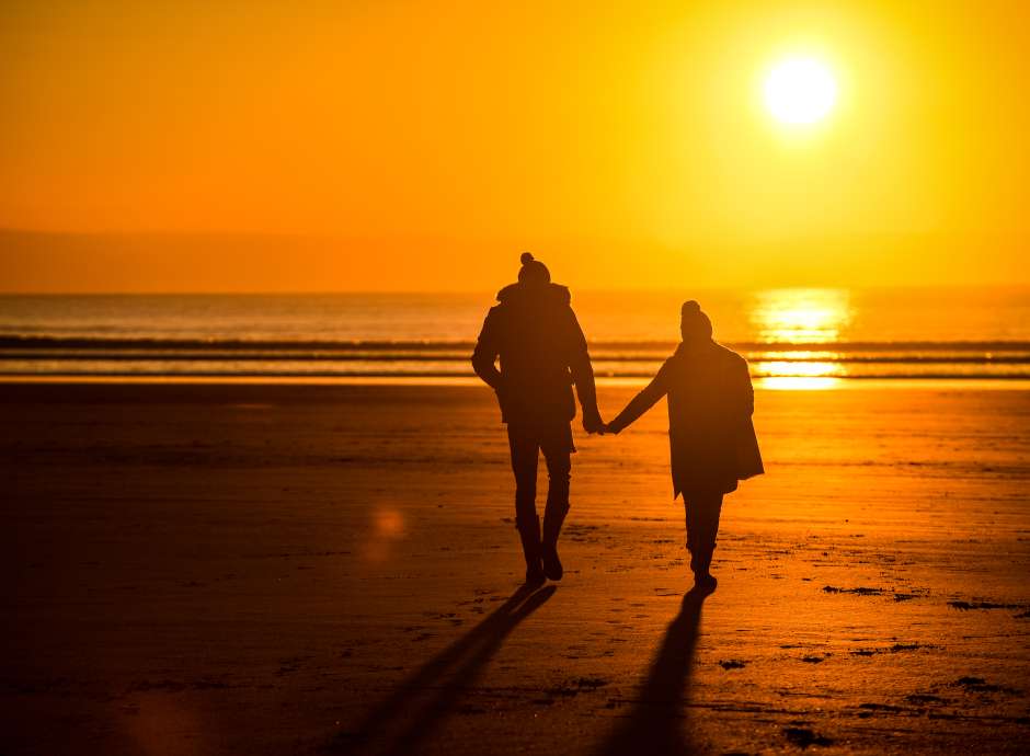 Couple walking on the beach during sunset at winter